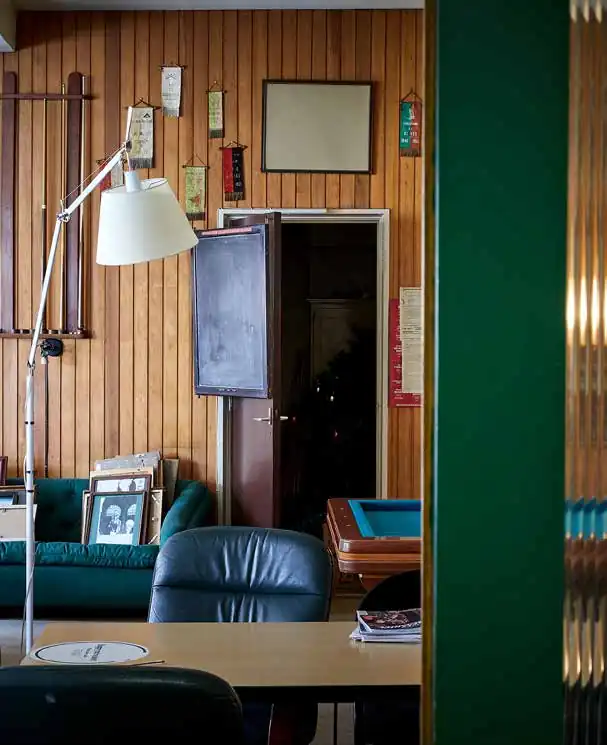 Interieur van een nostalgische ruimte aan de Ruysdaelkade met houten wandbekleding, leren stoelen, vintage decoraties en schilderijen tegen een groene bank.