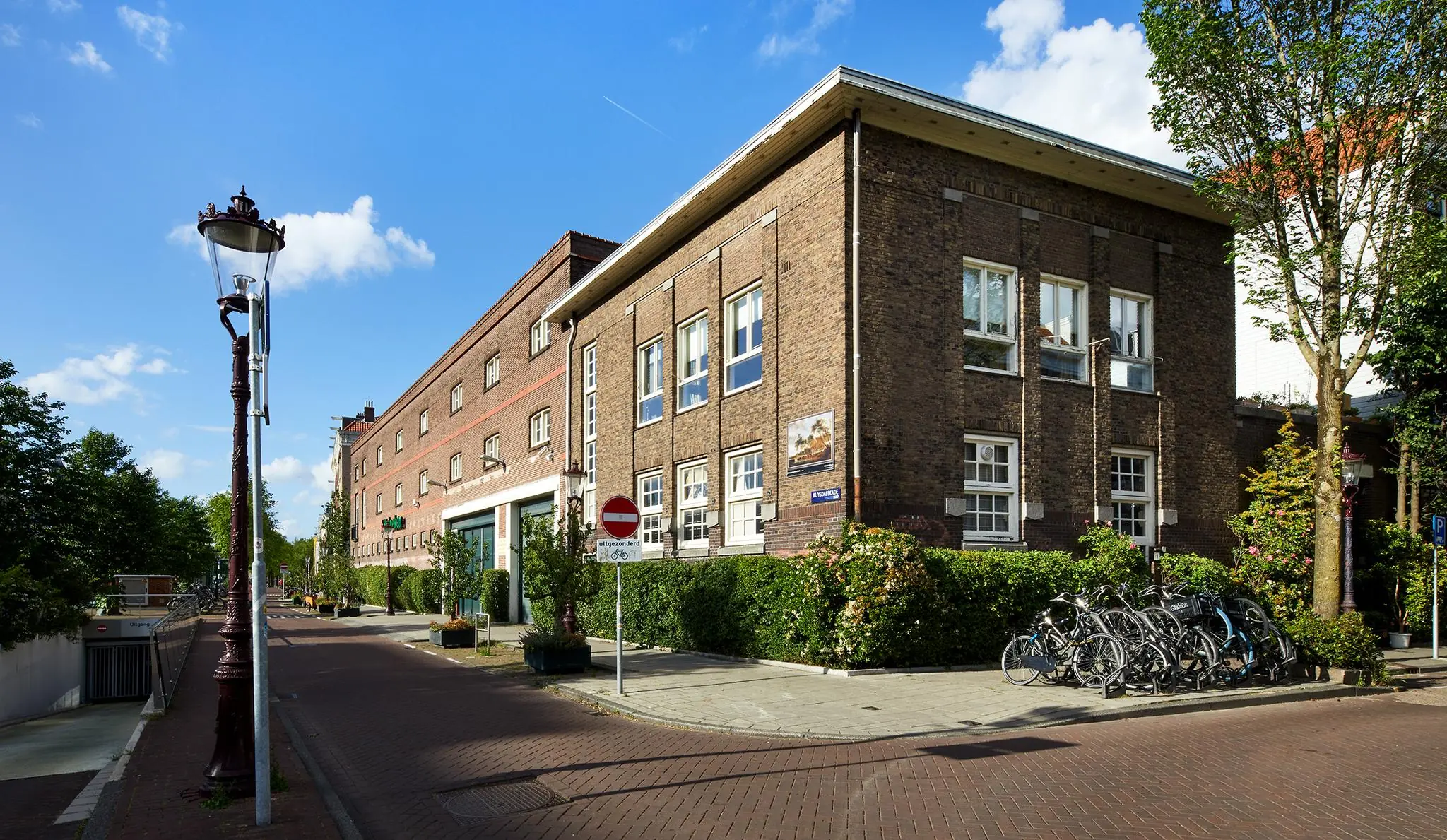 Straatbeeld van de Ruysdaelkade in Amsterdam met een bakstenen gebouw, fietsenrek en een eenrichtingsverkeersbord.