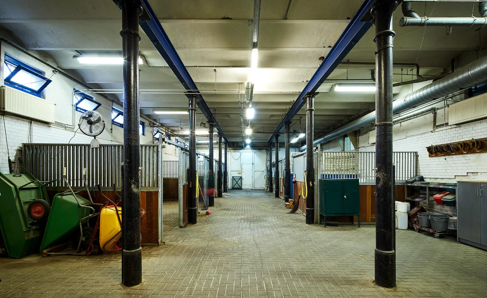 Binnenaanzicht van een verzorgde paardenstal aan de Ruysdaelkade met metalen hekken, schoonmaakmaterialen en opbergruimtes.