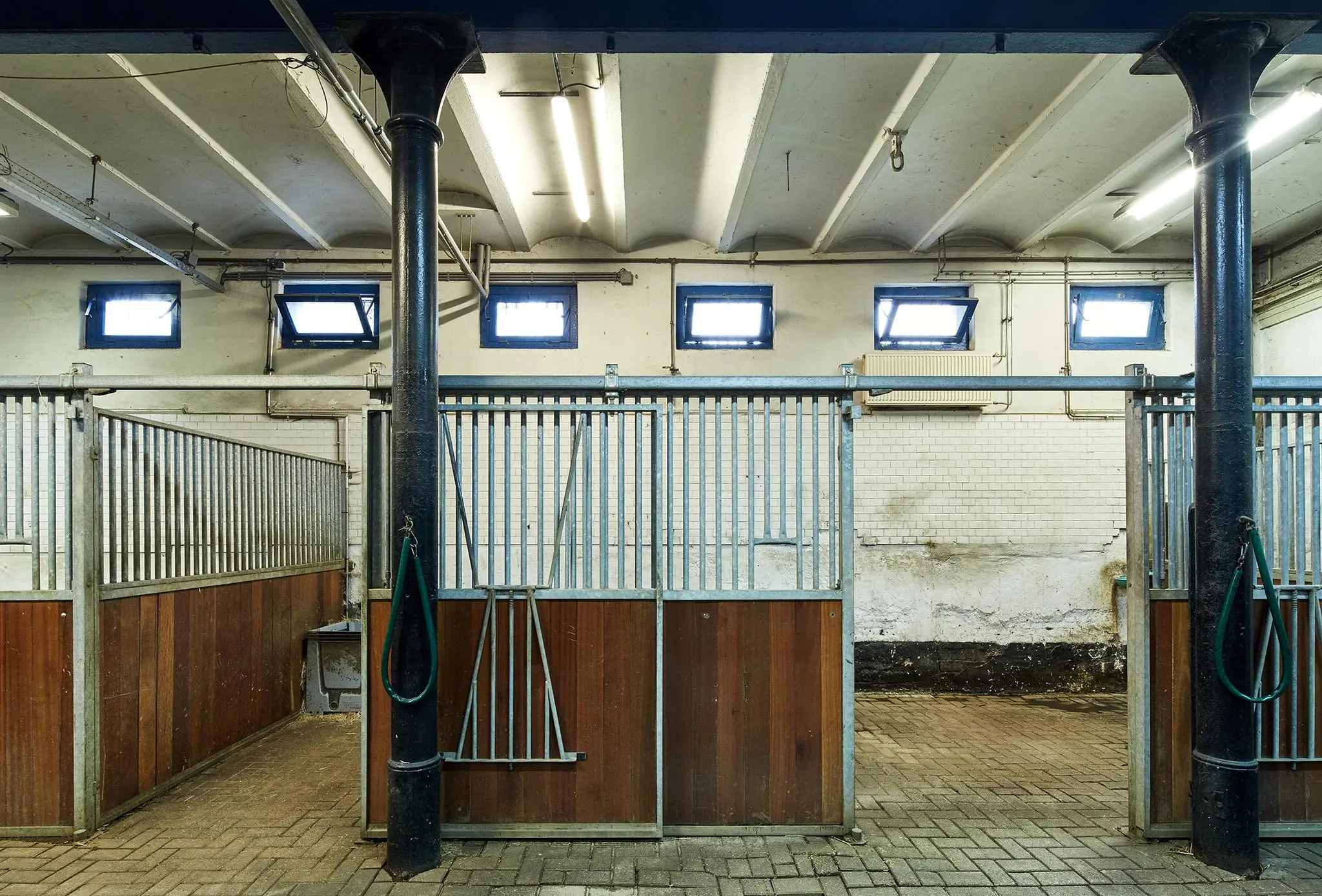 Binnenzicht van een paardenstal aan de Ruysdaelkade met metalen hekwerken, houten panelen en betonnen vloer.