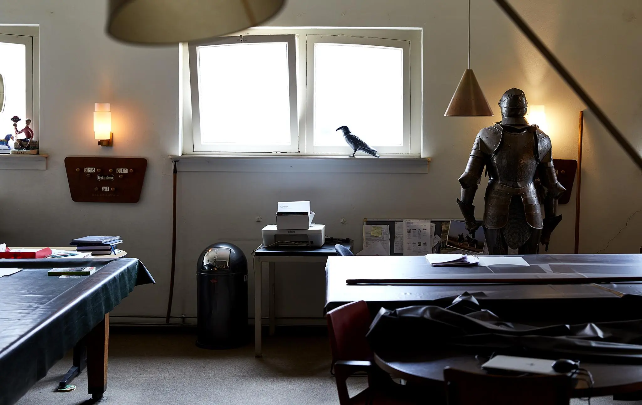 Een kantoorruimte aan de Ruysdaelkade met een ridderharnas, kraai op de vensterbank en een printer onder fel binnenvallend daglicht.