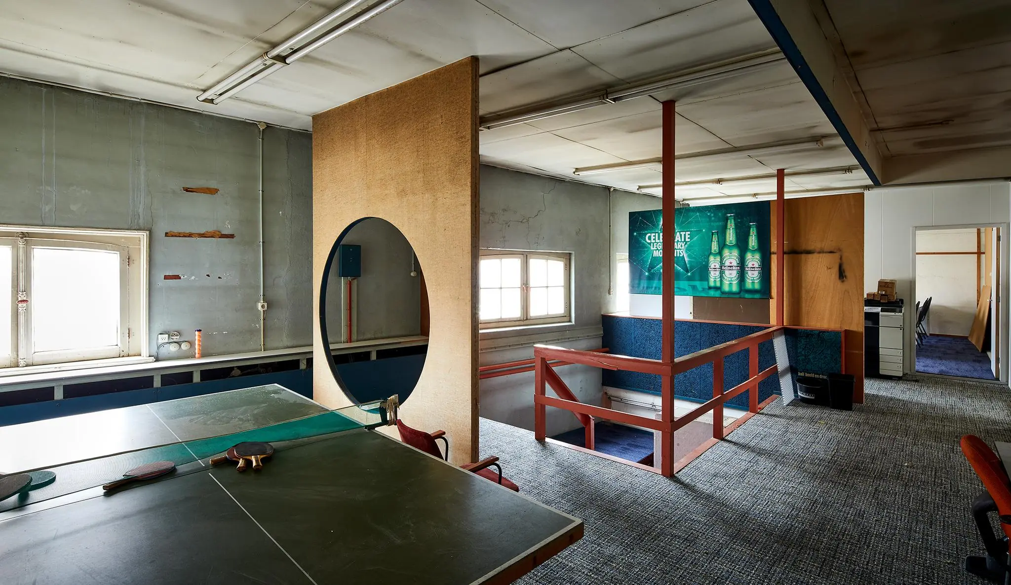 Verouderde kantoorruimte aan de Ruysdaelkade met een tafeltennistafel, scheidingswanden en een Heineken-poster aan de muur.