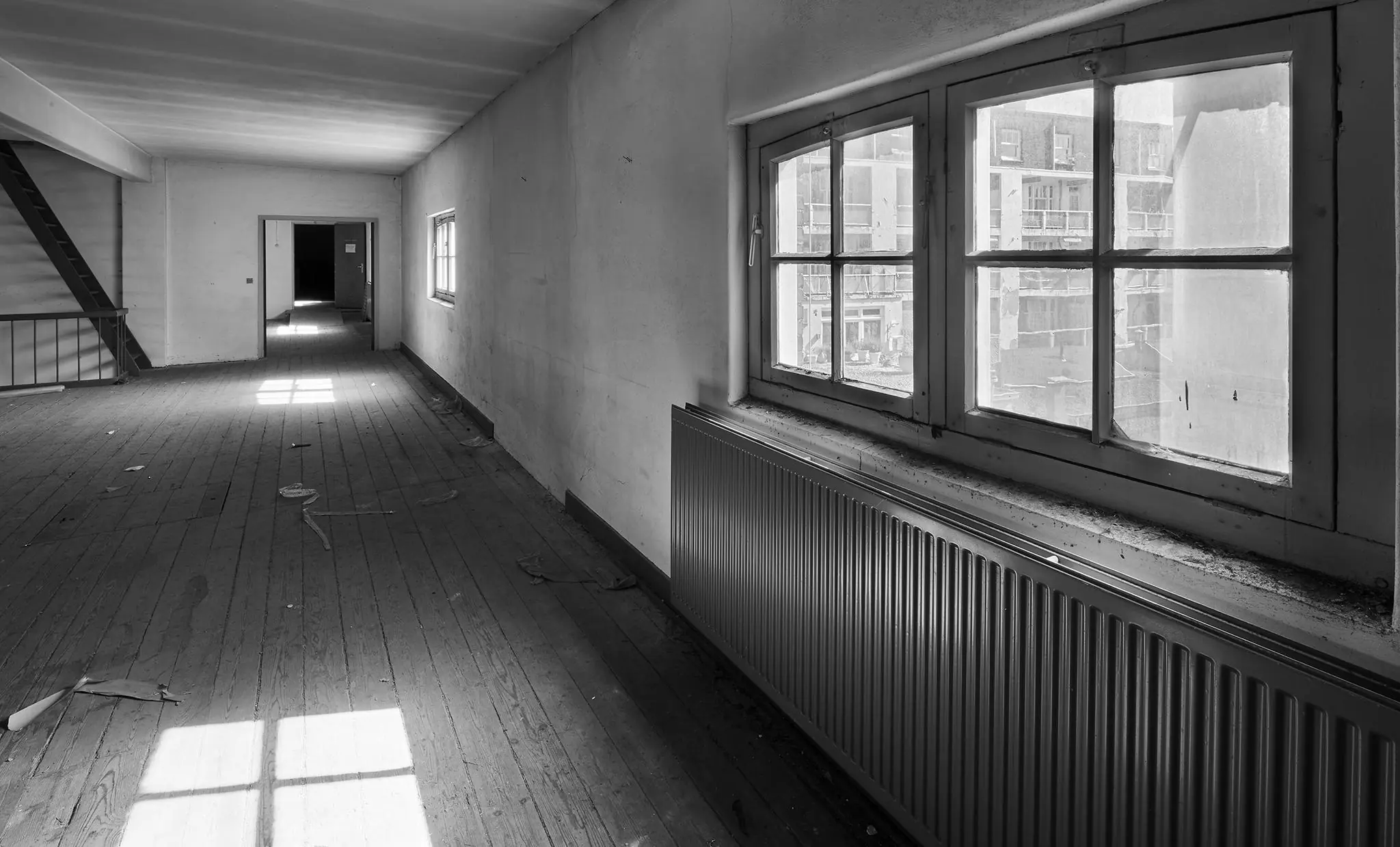 Zwart-witfoto van een lege, vervallen bovenverdieping aan de Ruysdaelkade met houten vloer, grote ramen en een metalen radiator.