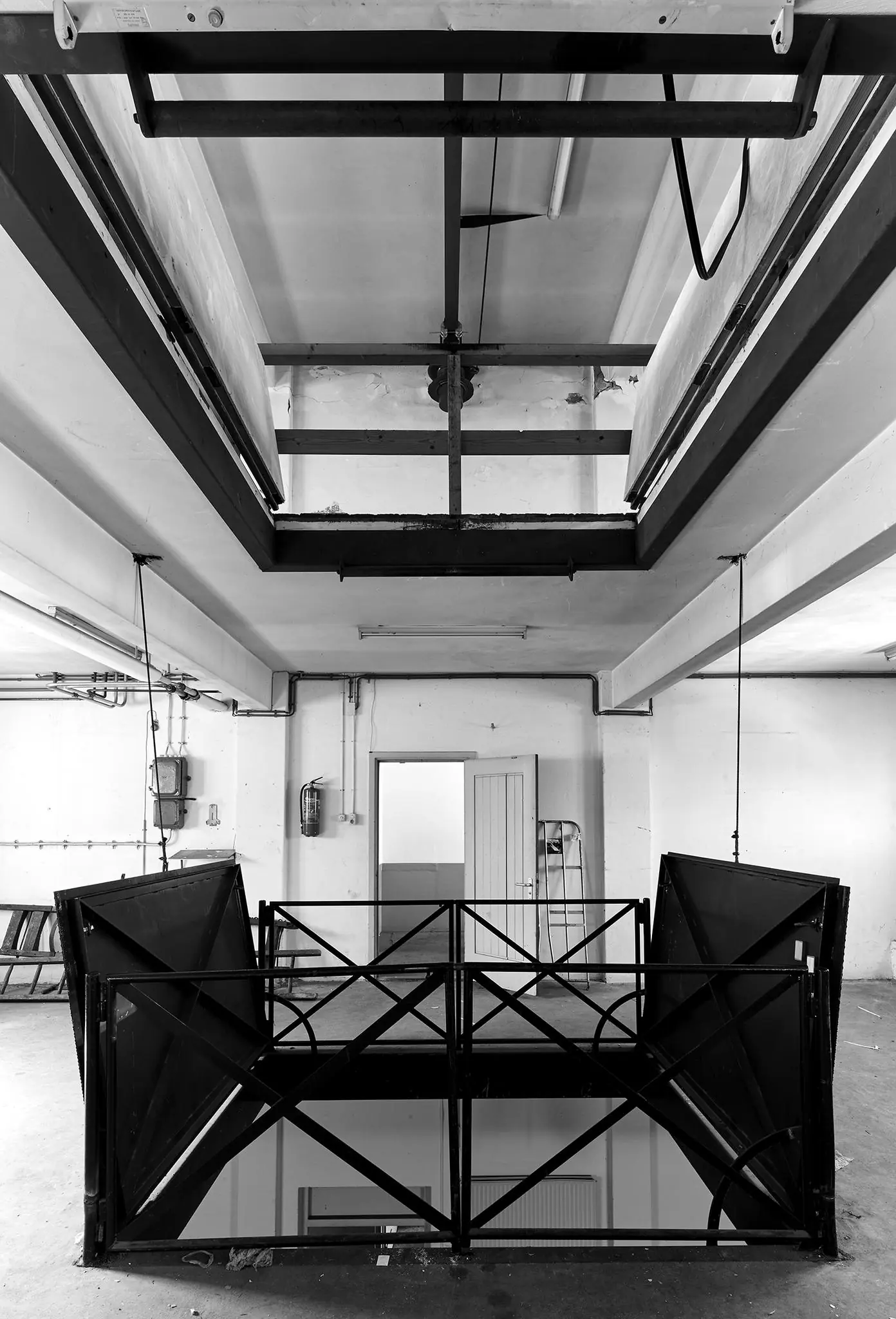 Zwart-witfoto van een industriële liftopening met metalen hekwerk in een leegstaande ruimte aan de Ruysdaelkade.