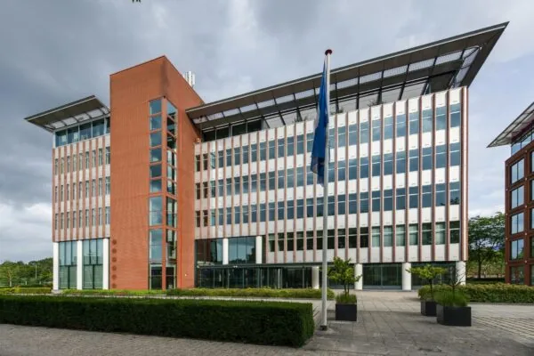 Modern kantoorgebouw aan de Lichtenauerlaan met glazen gevel, rode bakstenen toren en vlaggenmast op de voorgrond.