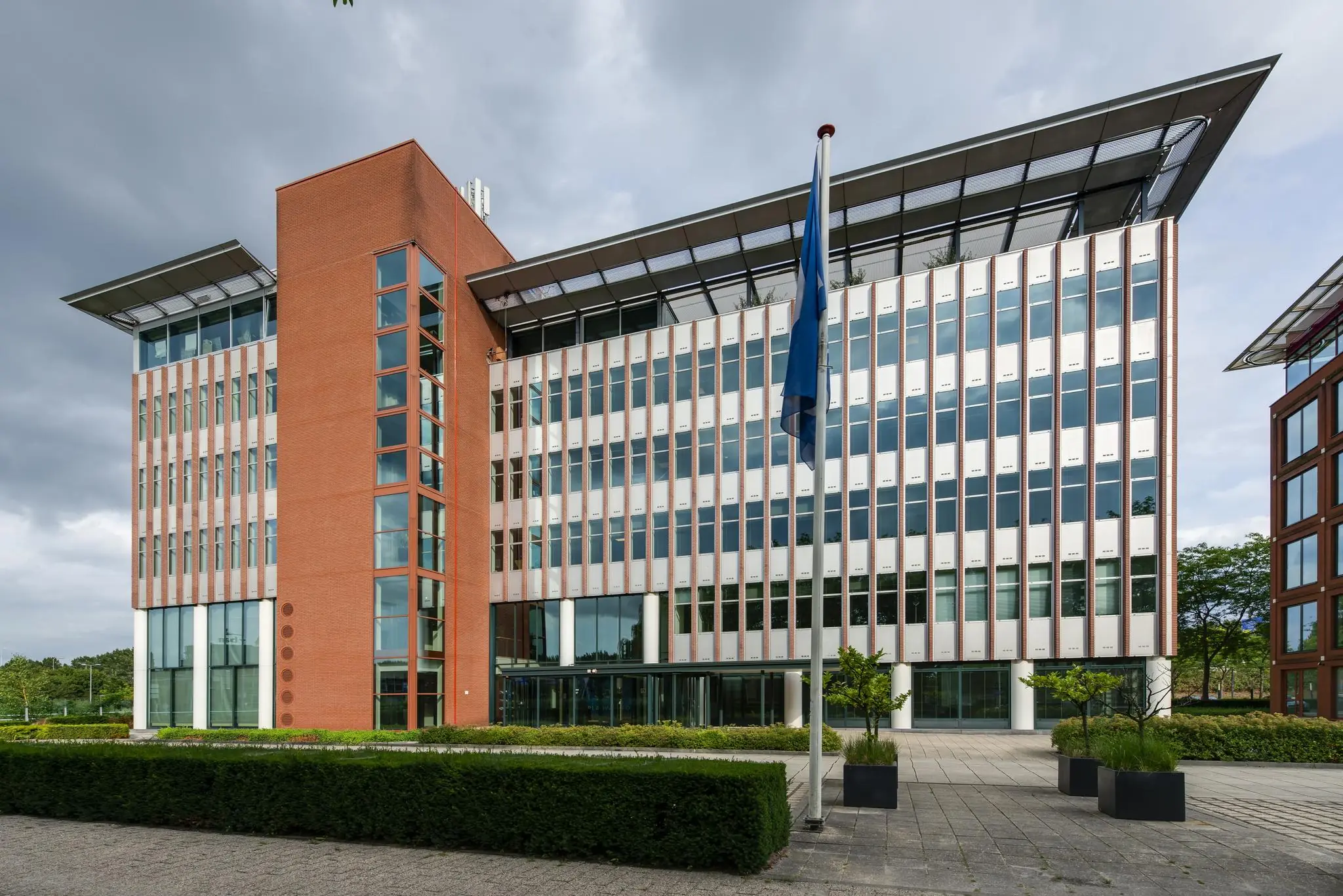 Modern kantoorgebouw aan de Lichtenauerlaan met glazen gevel, rode bakstenen toren en vlaggenmast op de voorgrond.