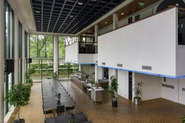 Moderne bedrijfskantine aan de Lichtenauerlaan met grote ramen, lange eettafels en een open keuken.