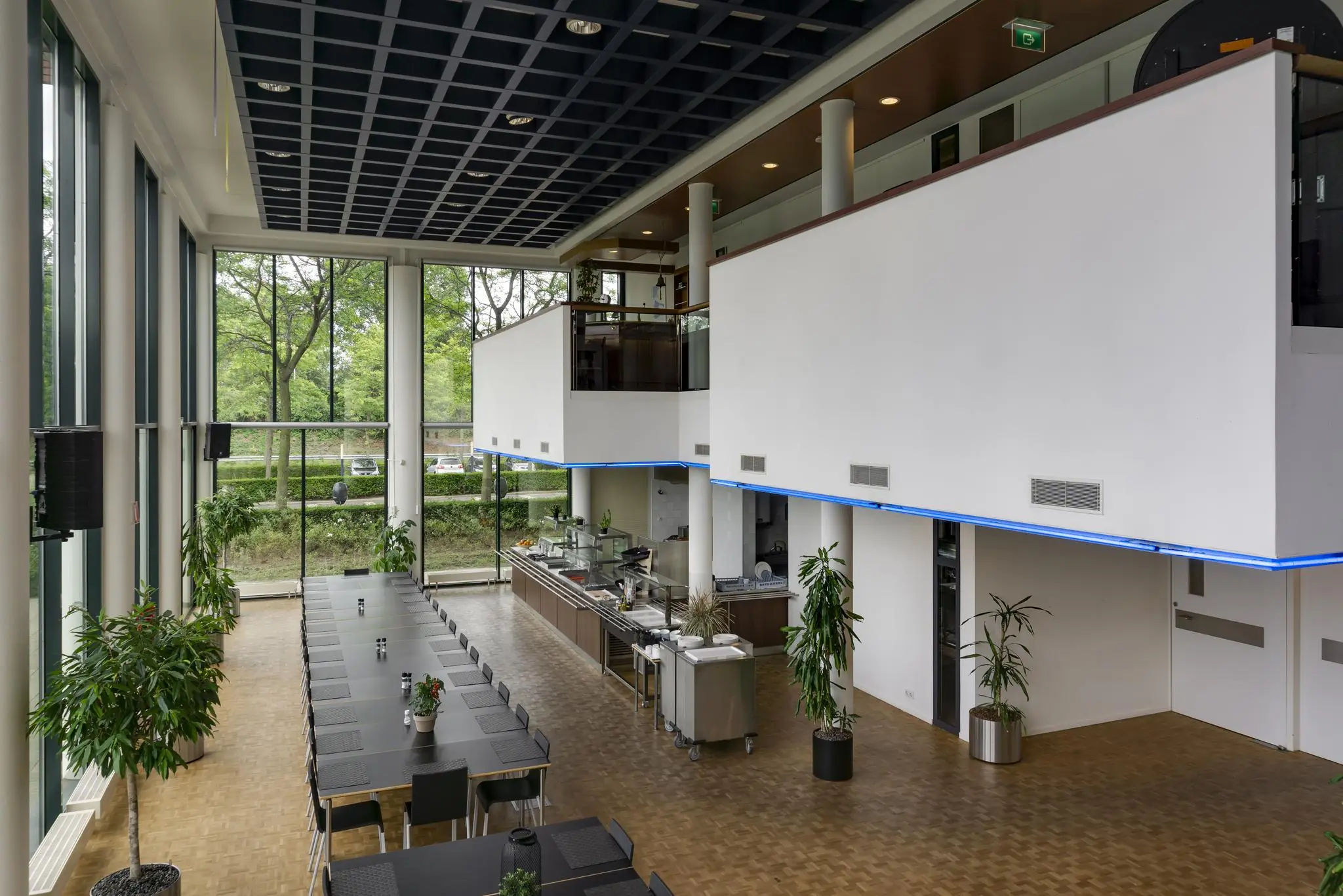 Moderne bedrijfskantine aan de Lichtenauerlaan met grote ramen, lange eettafels en een open keuken.