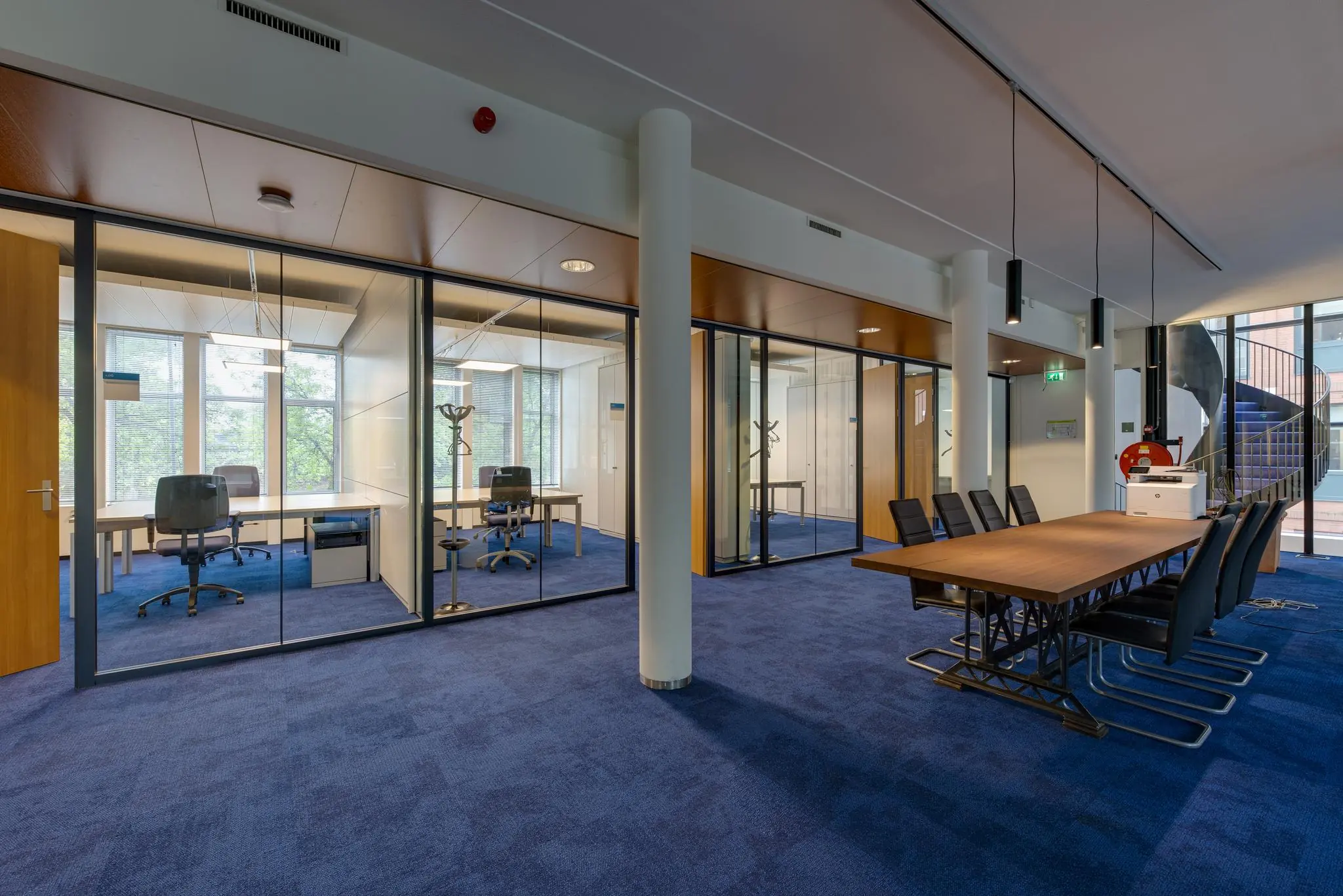Moderne kantoorruimte aan de Lichtenauerlaan met glazen vergaderruimtes, blauwe vloerbedekking en een grote vergadertafel.
