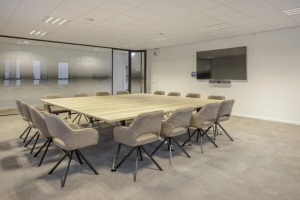 Vergaderruimte aan de Hiridostraat met een grote houten tafel, zestien stoelen en een flatscreen aan de muur.