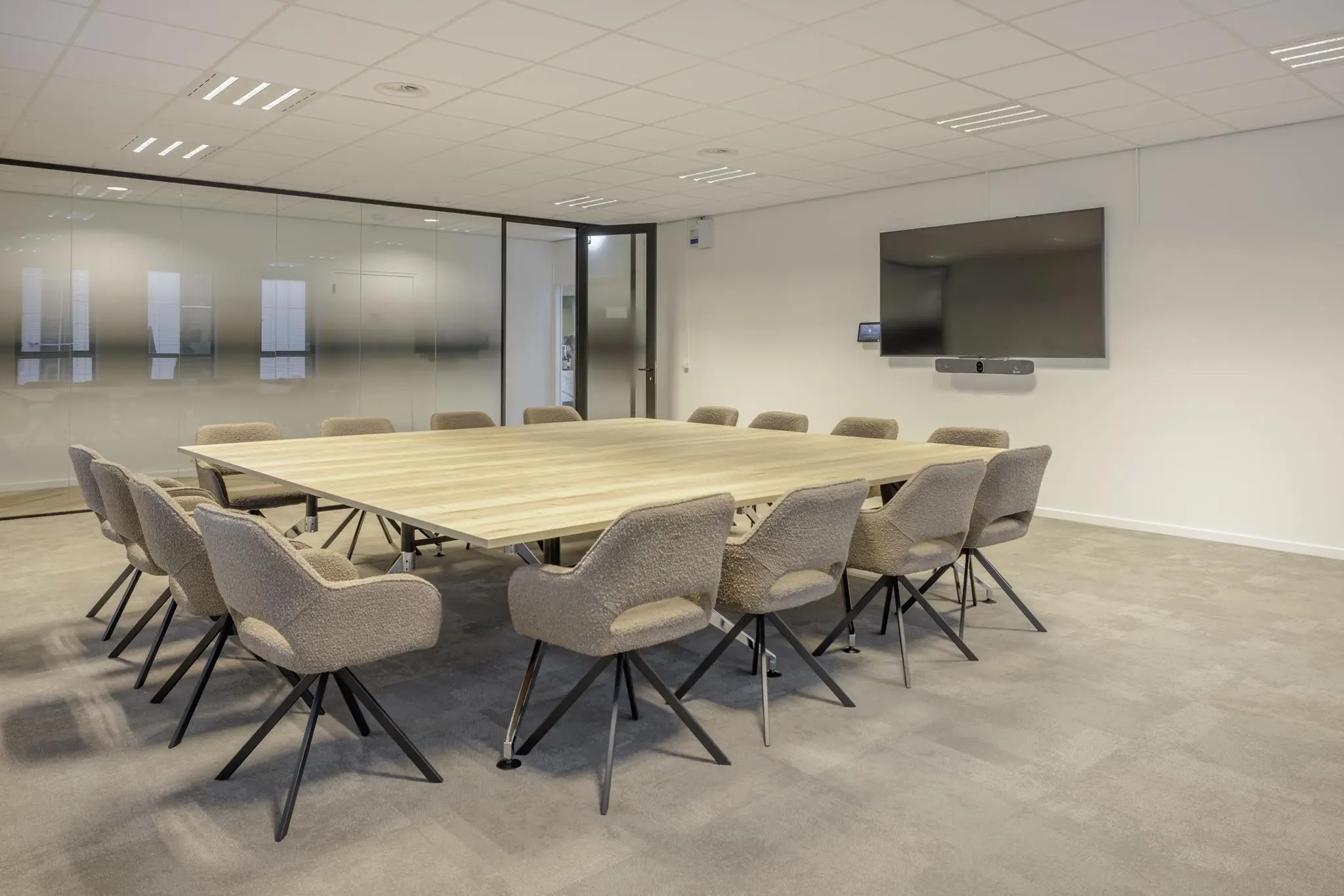 Vergaderruimte aan de Hiridostraat met een grote houten tafel, zestien stoelen en een flatscreen aan de muur.