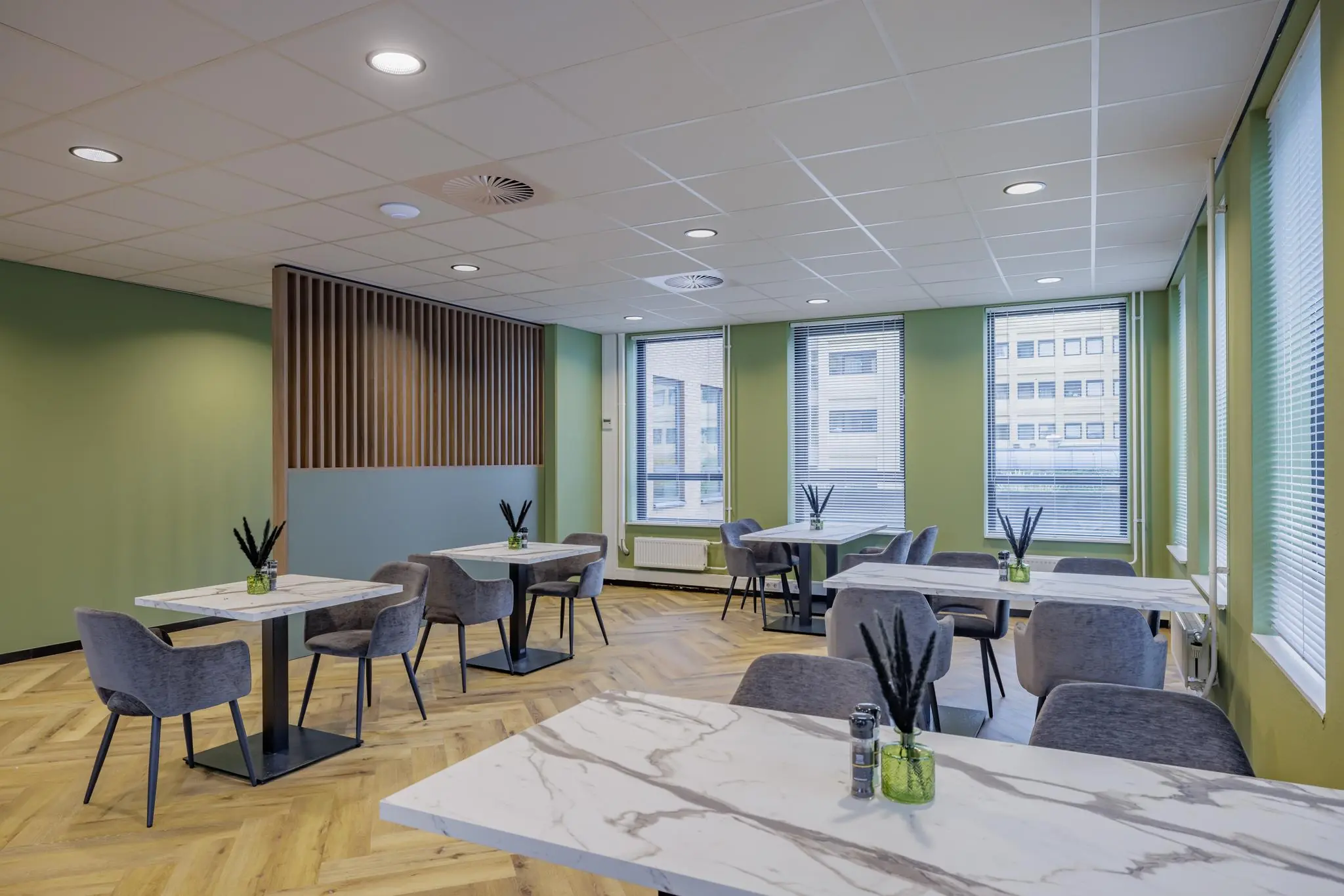 Moderne, lichtgroene lunchruimte aan de Hiridostraat met marmeren tafels, grijze stoelen en grote ramen.