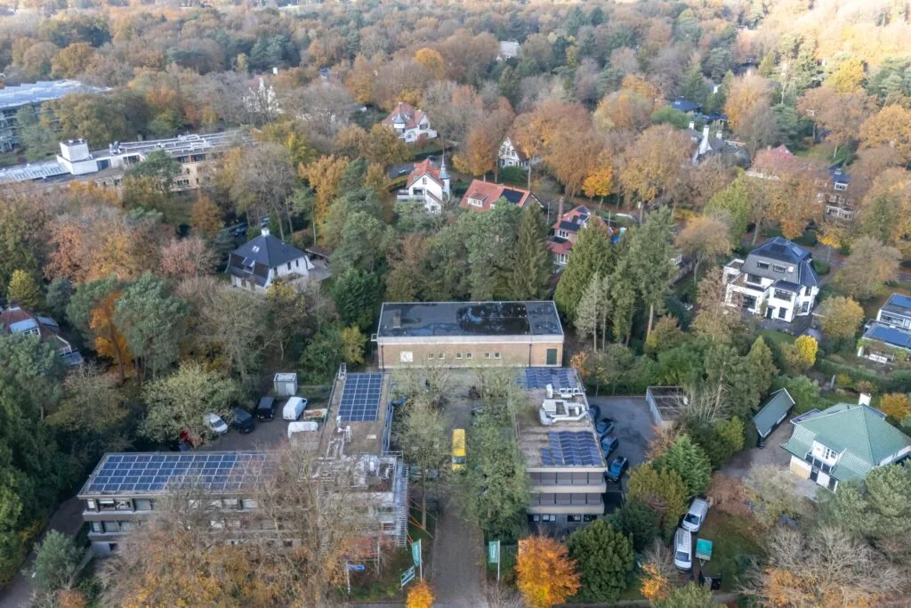 Luchtfoto van een gebouwencomplex aan de Rembrandtlaan, omringd door bomen en woonhuizen in herfstkleuren.