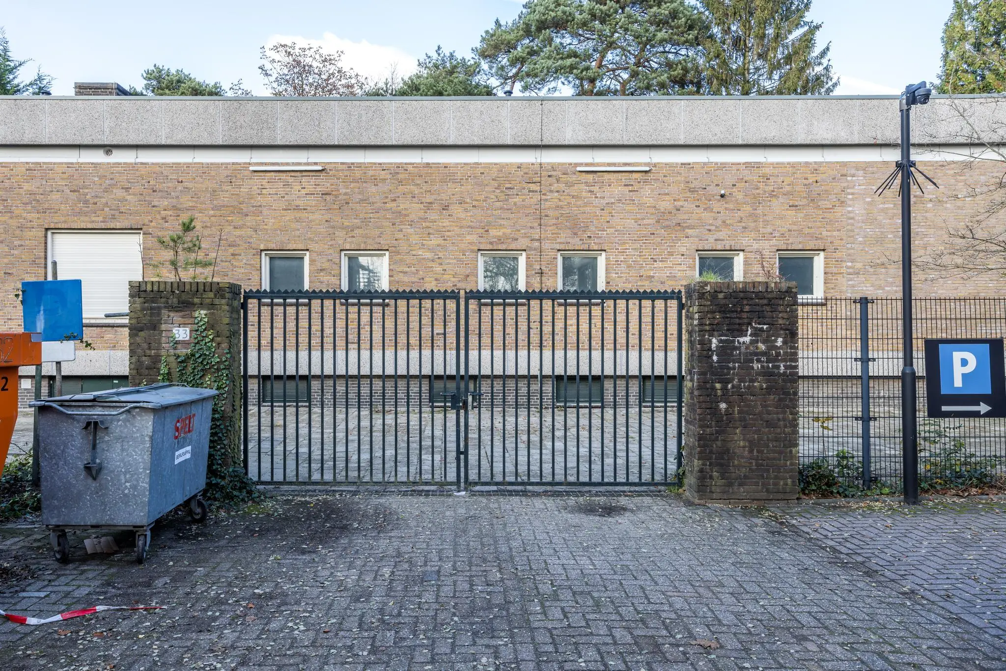 Afgesloten toegangshek voor een bakstenen gebouw aan de Rembrandtlaan, met een parkeerbord en afvalcontainer op de voorgrond.
