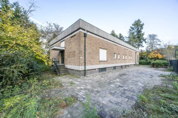 Hoekaanzicht van een vrijstaand, laagbouw bakstenen gebouw aan de Rembrandtlaan met betegelde oprit en omringend groen.