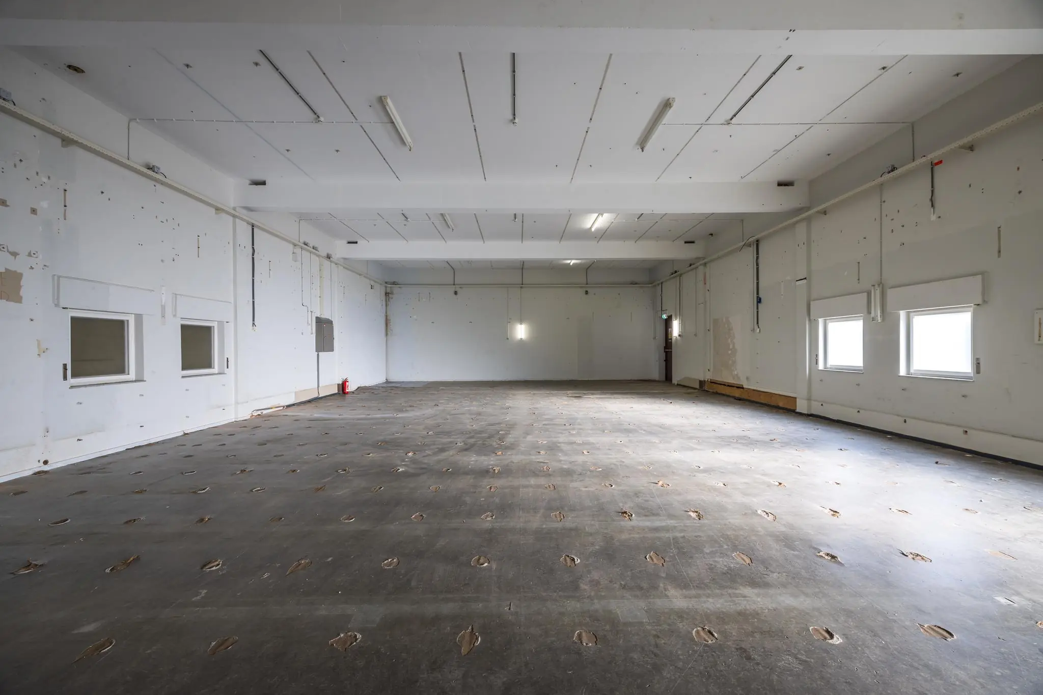 Lege industriële ruimte aan de Rembrandtlaan met beschadigde vloer en zicht op witte muren en ramen.