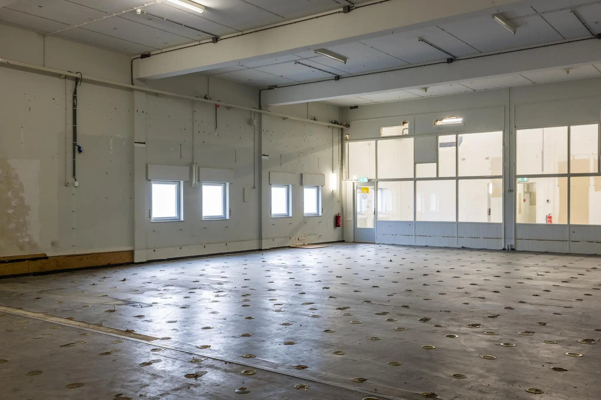 Leegstaand industrieel interieur aan de Rembrandtlaan met betonnen vloer, ramen en kunstlicht.