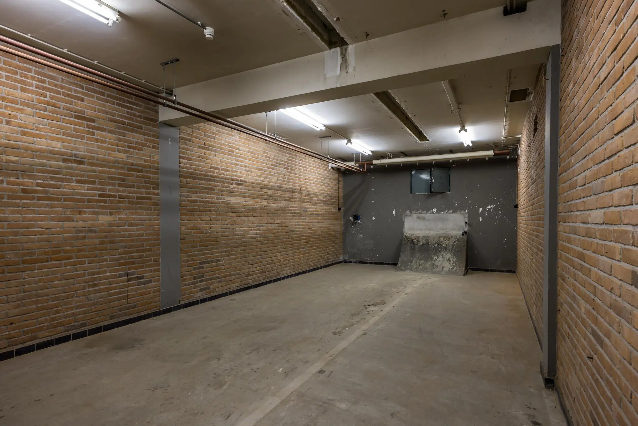 Lege, smalle garageruimte met bakstenen muren en betonnen vloer aan de Rembrandtlaan.