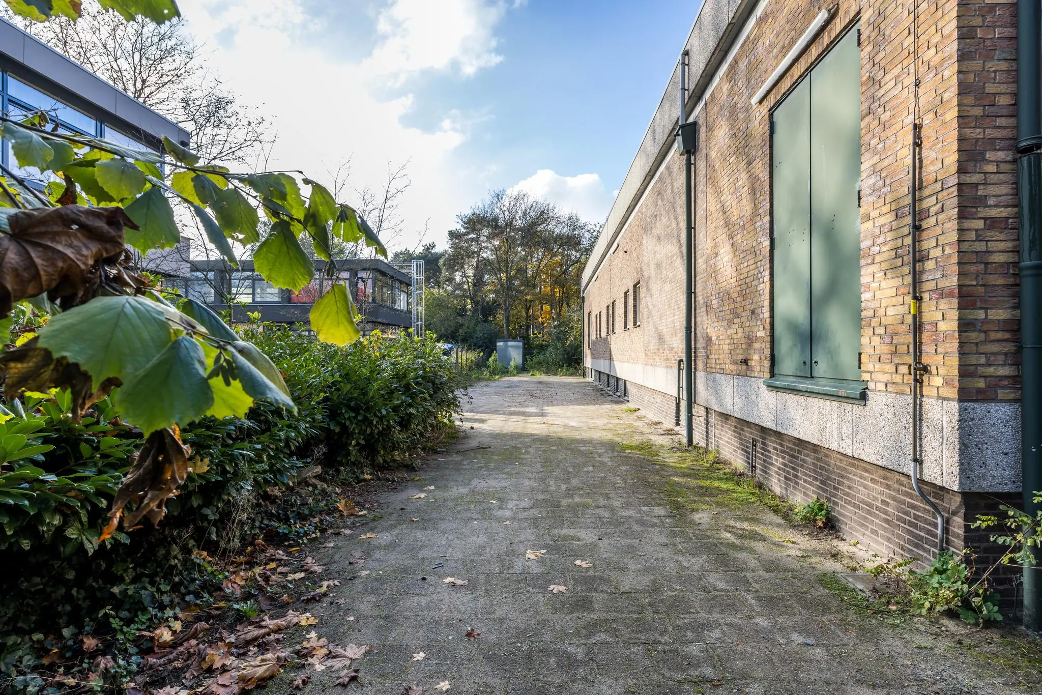 Bestrate achterzijde van een bakstenen gebouw aan de Rembrandtlaan, omgeven door groen en moderne bebouwing.
