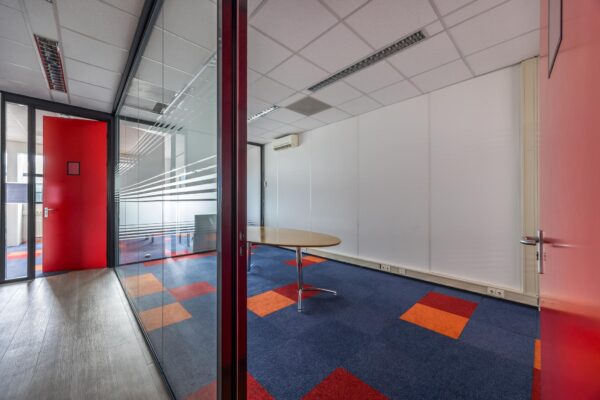 Vergaderruimte met glazen wand, kleurrijk tapijt en een ovale tafel in een kantoor aan de Atoomweg.
