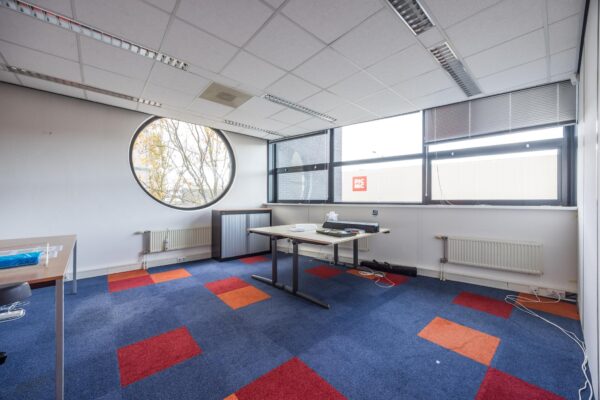 Kantoorruimte aan de Atoomweg met kleurrijke vloerbedekking, ronde raamopening en uitzicht op een Picnic-gebouw.