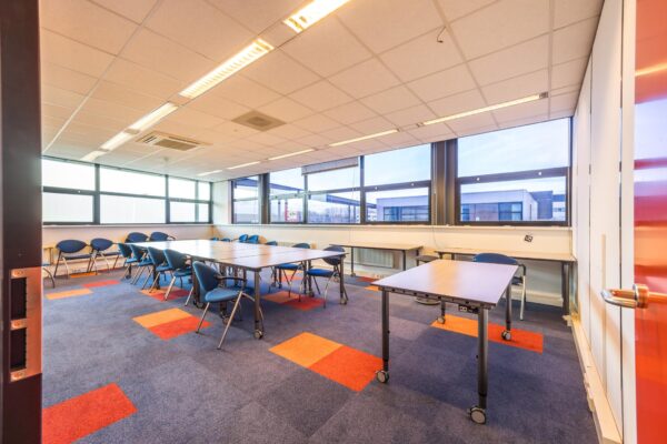 Vergaderruimte aan de Atoomweg met opklapbare tafels, blauwe stoelen en grote ramen met uitzicht op kantoorgebouwen.