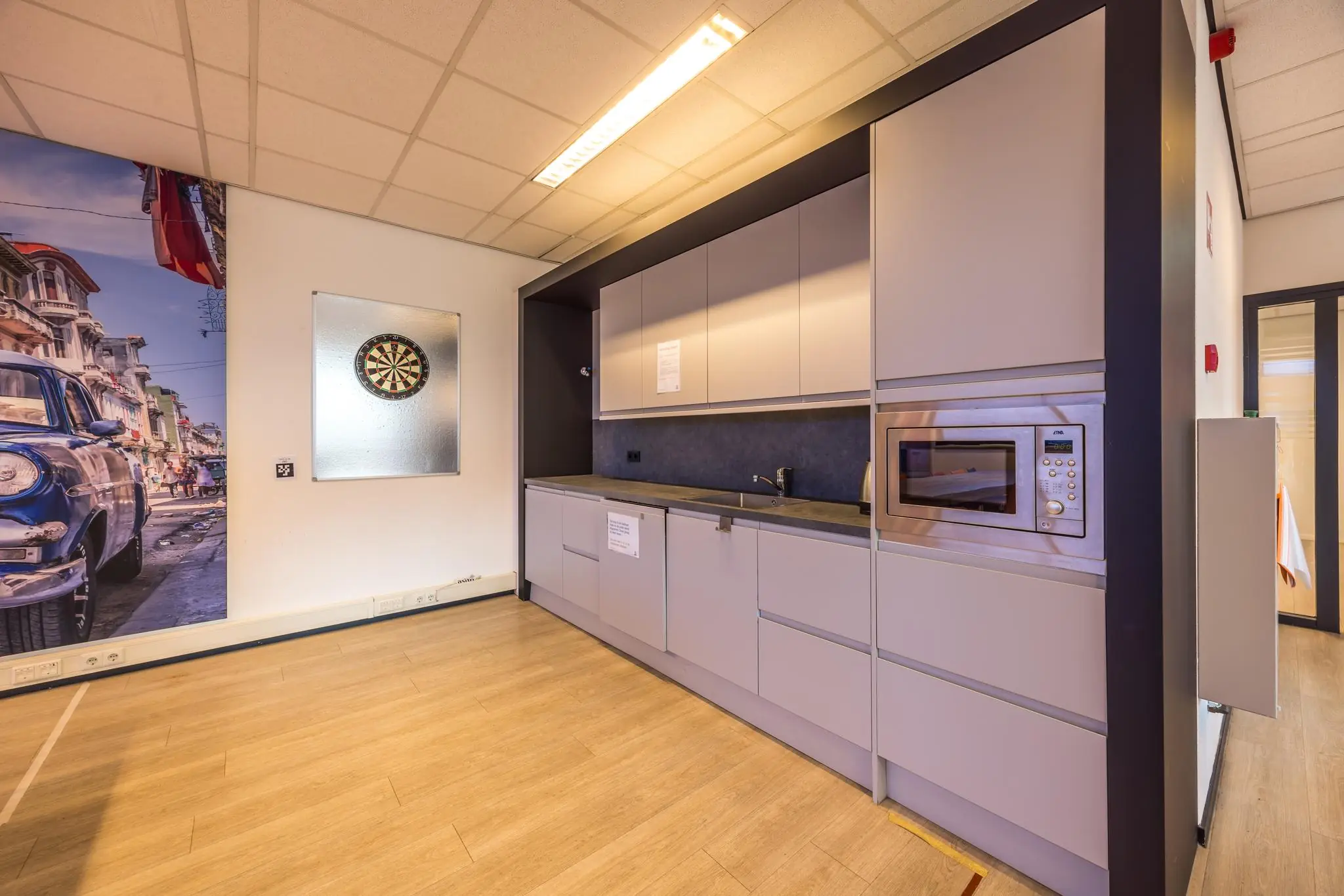 Moderne kantoorkeuken met grijze kasten, ingebouwde magnetron en een dartbord aan de muur.