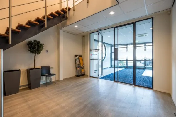 Ingangshal van een modern kantoorpand aan de Atoomweg met glazen schuifdeuren, een trap en wachtruimte.