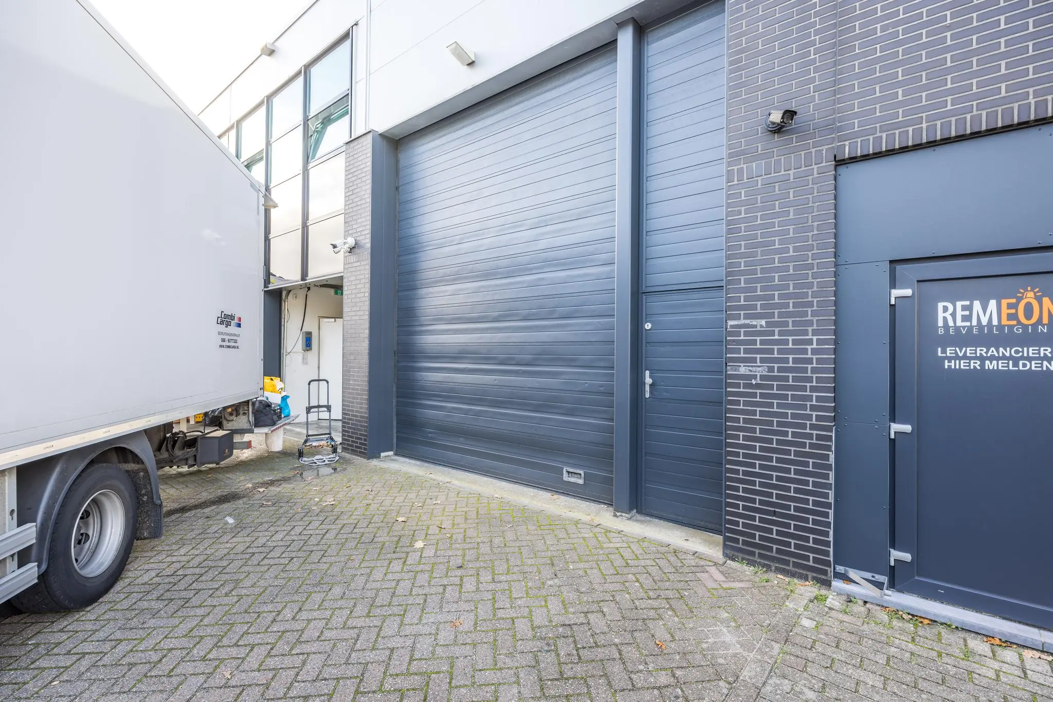 Achterzijde van een bedrijfspand aan de Atoomweg met een laadperron, vrachtwagen en ingang voor leveranciers van Remeon Beveiliging.