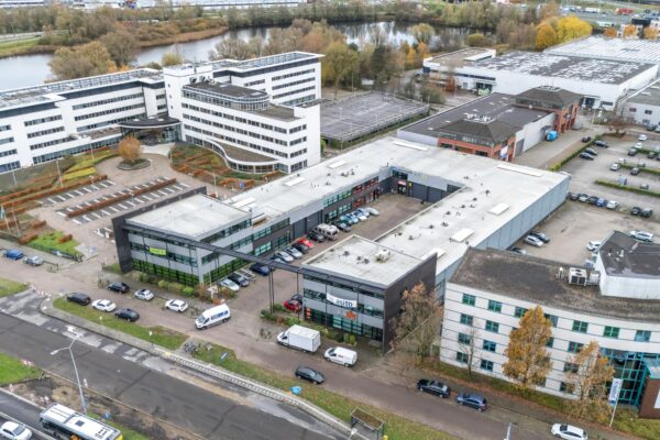 Luchtfoto van een bedrijfsverzamelgebouw aan de Atoomweg met omliggende kantoren, parkeerplaatsen en een waterpartij op de achtergrond.
