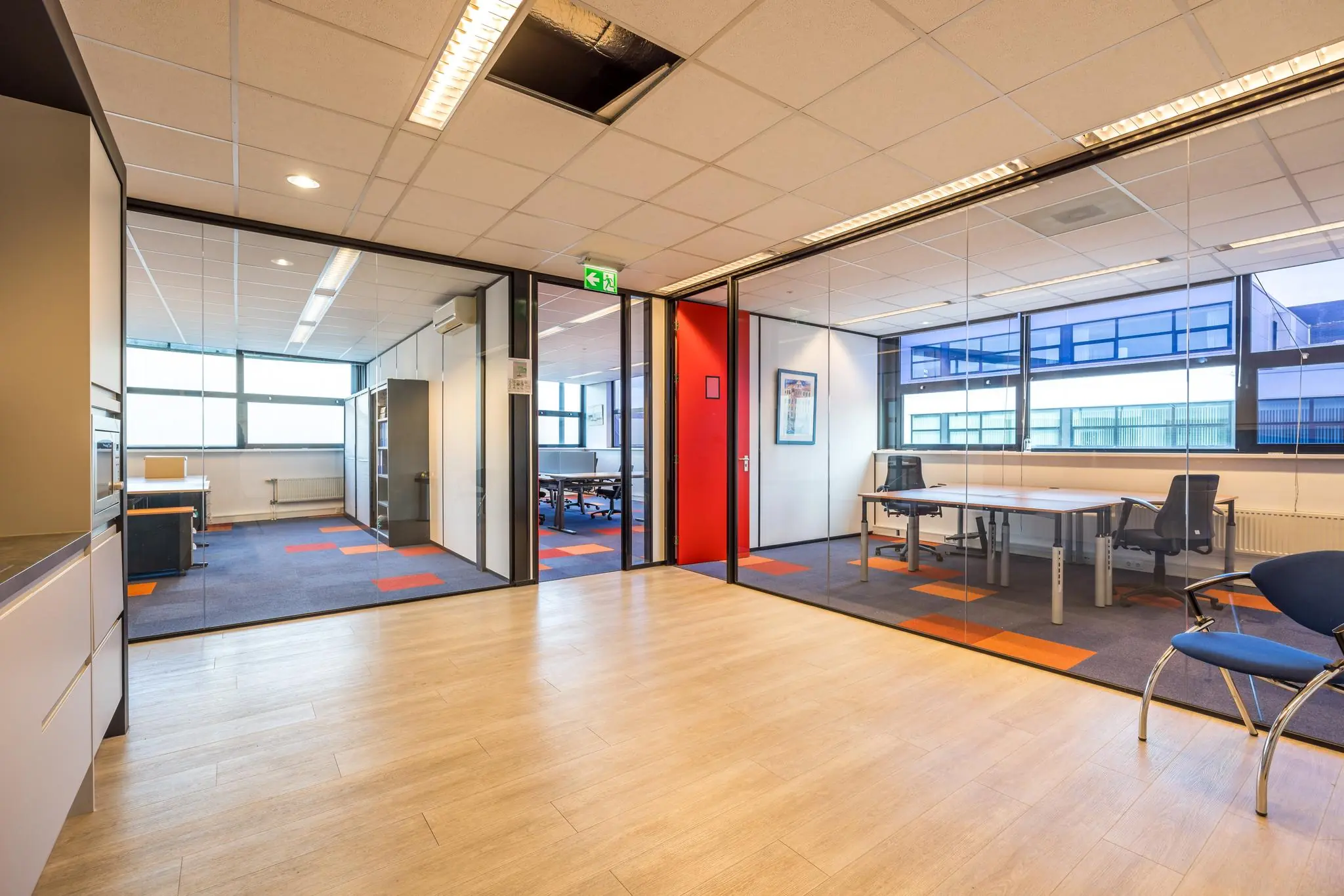 Moderne kantoorruimte aan de Atoomweg met glazen wanden, bureaus en opvallende rood-blauwe vloerbedekking.
