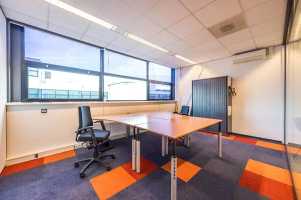 Modern kantoor met grote ramen, felgekleurd tapijt en twee bureaus in bedrijfsverzamelgebouw aan de Atoomweg.
