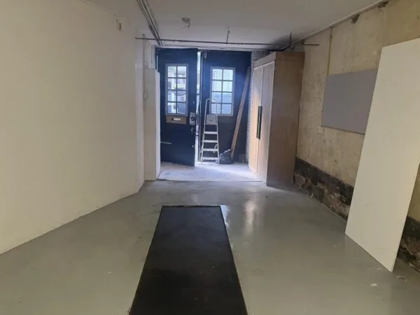 Lege, deels gerenoveerde ruimte aan de Nobeldwarsstraat met betonnen vloer, houten kast en open deur naar buiten.