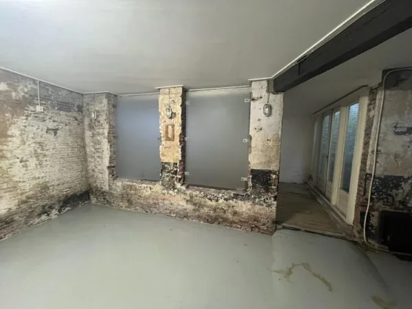 Kelderruimte aan de Nobeldwarsstraat met deels afgebladderde bakstenen muren, betonnen vloer en matglasramen.