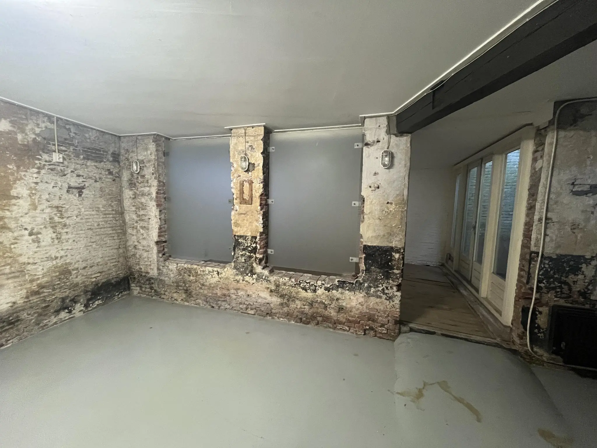 Kelderruimte aan de Nobeldwarsstraat met deels afgebladderde bakstenen muren, betonnen vloer en matglasramen.