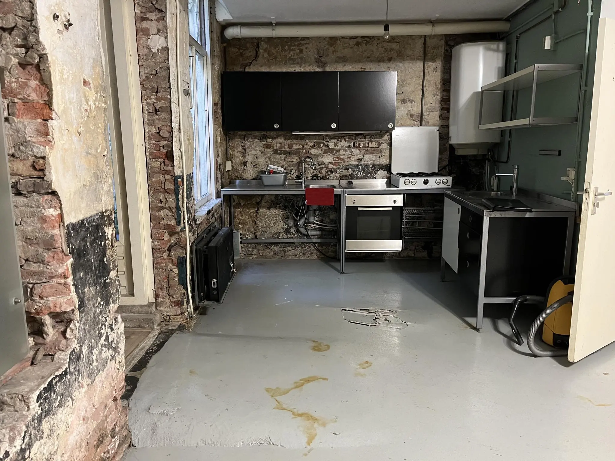 Industriële keuken in de Nobeldwarsstraat met zichtbare bakstenen muren, metalen aanrecht en versleten betonnen vloer.