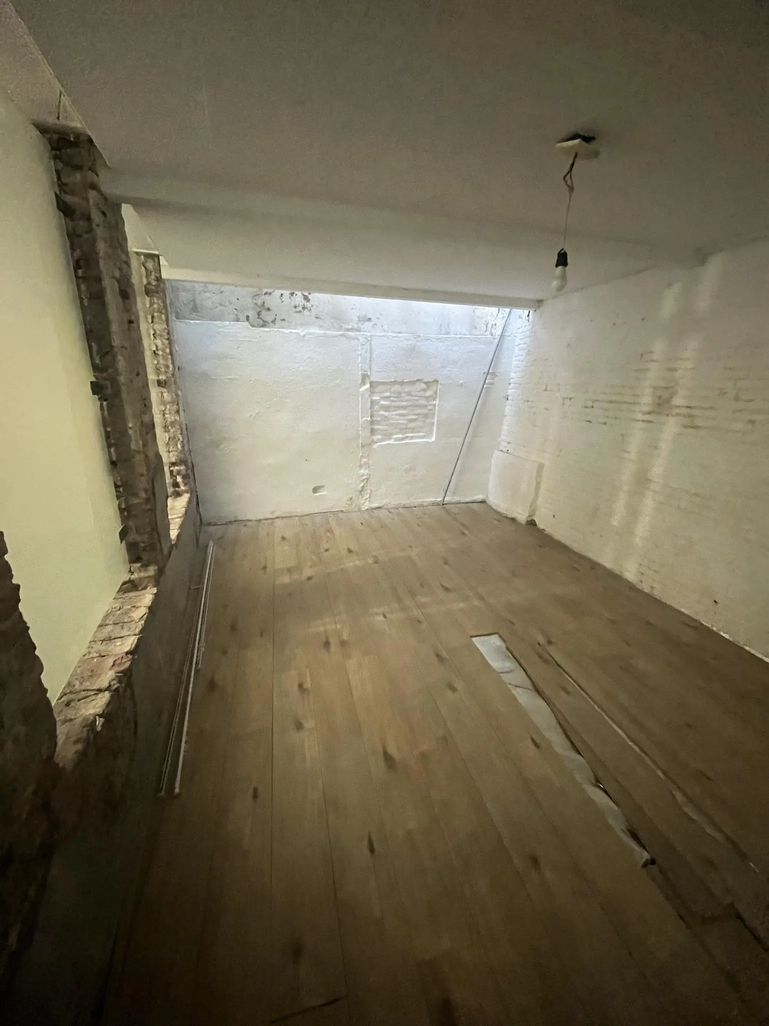 Donkere kamer aan de Nobeldwarsstraat met houten vloer, beschadigde planken en onafgewerkte muren.
