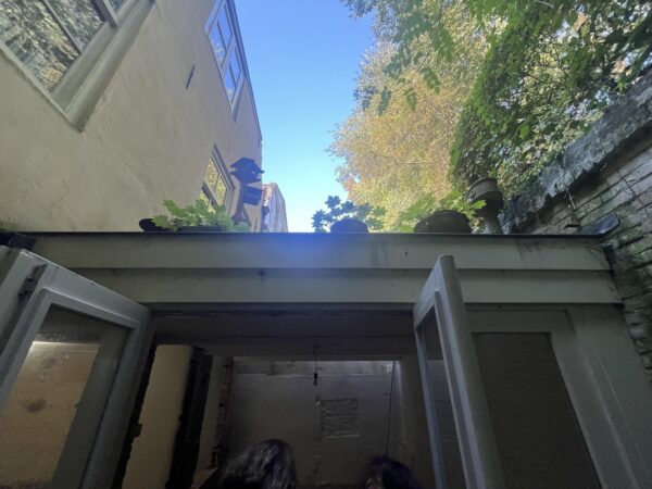 Doorkijk naar de lucht vanaf een binnenplaats aan de Nobelstraat, met plantenbakken en vogelhuisjes op een afdak.