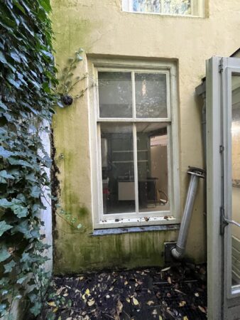 Achtergevel van een gebouw aan de Nobeldwarsstraat met een vervuild raam, klimop en een afvoerpijp.