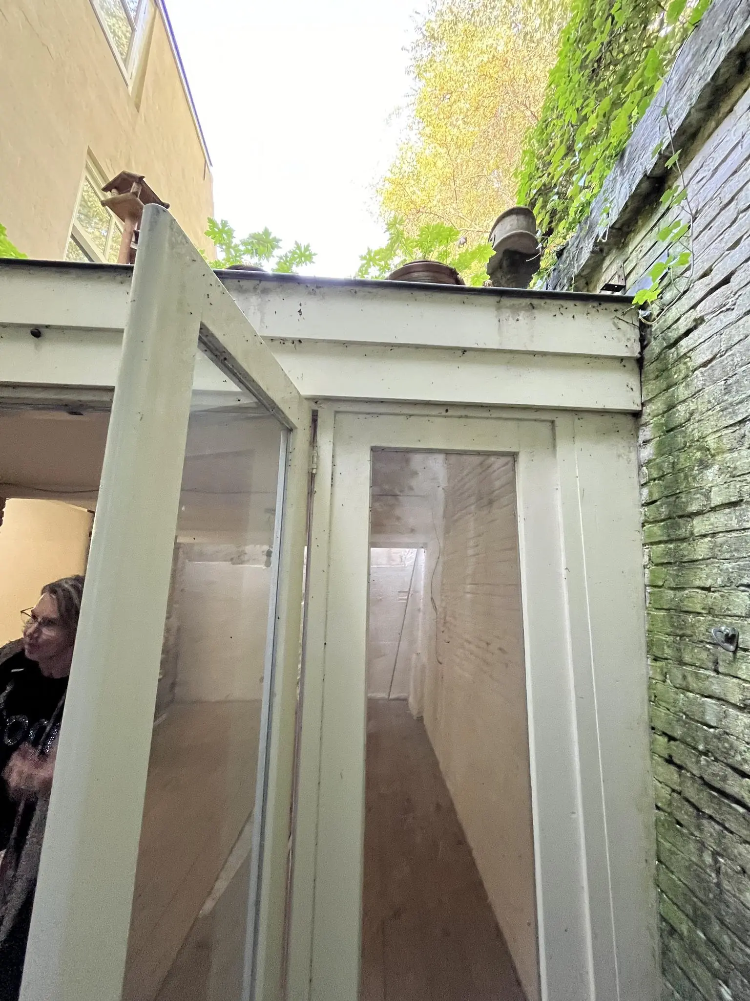 Smalle doorgang met glazen deuren en witte muren in een steegje aan de Nobeldwarsstraat, met planten en oude objecten op het dak.