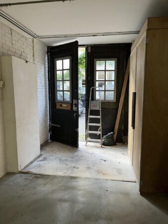 Binnenruimte met openstaande zwarte houten deuren aan de Nobeldwarsstraat, een ladder en bouwmaterialen bij de uitgang.