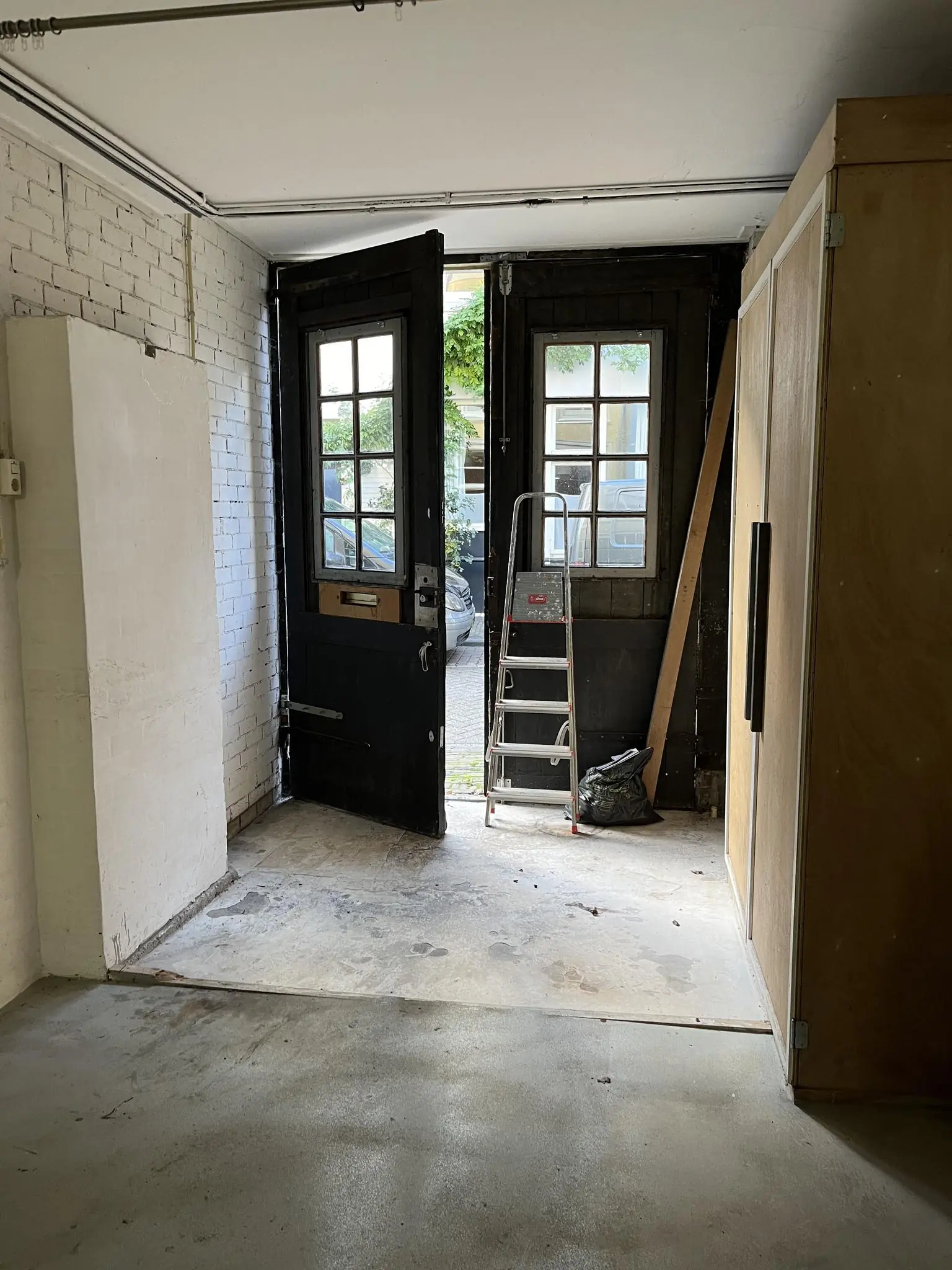 Binnenruimte met openstaande zwarte houten deuren aan de Nobeldwarsstraat, een ladder en bouwmaterialen bij de uitgang.