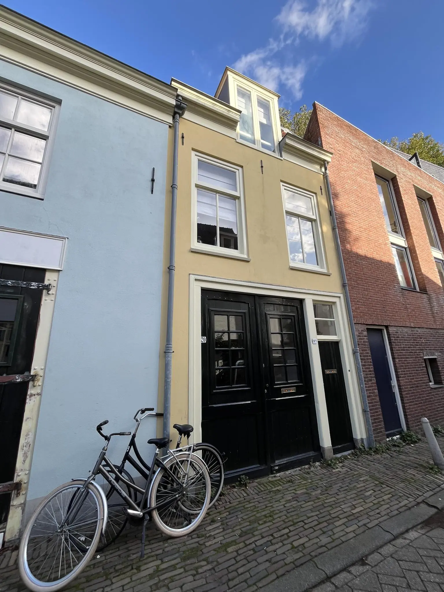 Geel woonhuis aan de Nobeldwarsstraat met zwarte dubbele deur en twee fietsen ervoor.