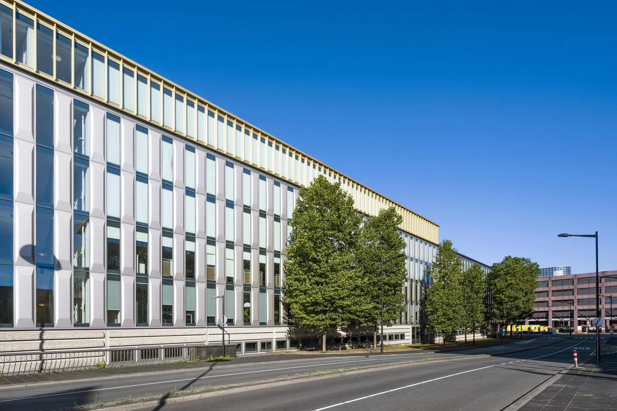 Modern kantoorgebouw aan de Hoekenrode in Amsterdam, met glasgevel en bomen langs de straat.