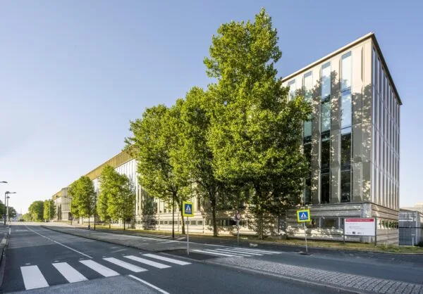Modern kantoorgebouw aan de Hoekenrode in Amsterdam met bomen en een zebrapad op de voorgrond.