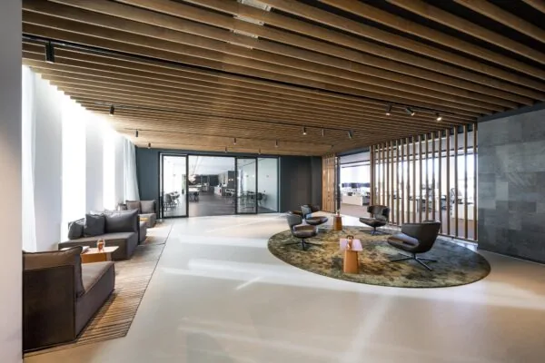 Moderne wachtruimte in kantoorgebouw Hoekenrode met loungestoelen, houten plafond en glazen vergaderruimtes.