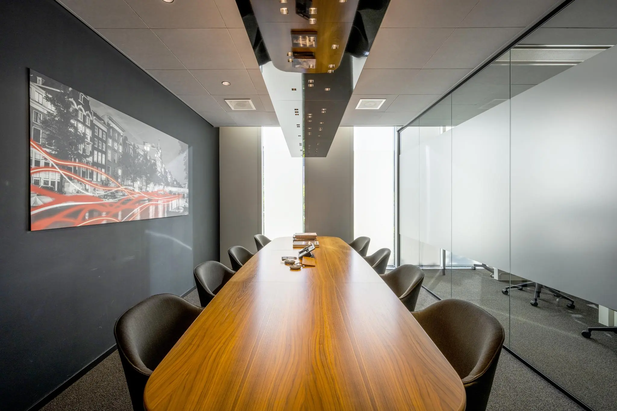Moderne vergaderruimte in Hoekenrode met lange houten tafel, glazen wanden en kunstwerk van Amsterdam aan de muur.