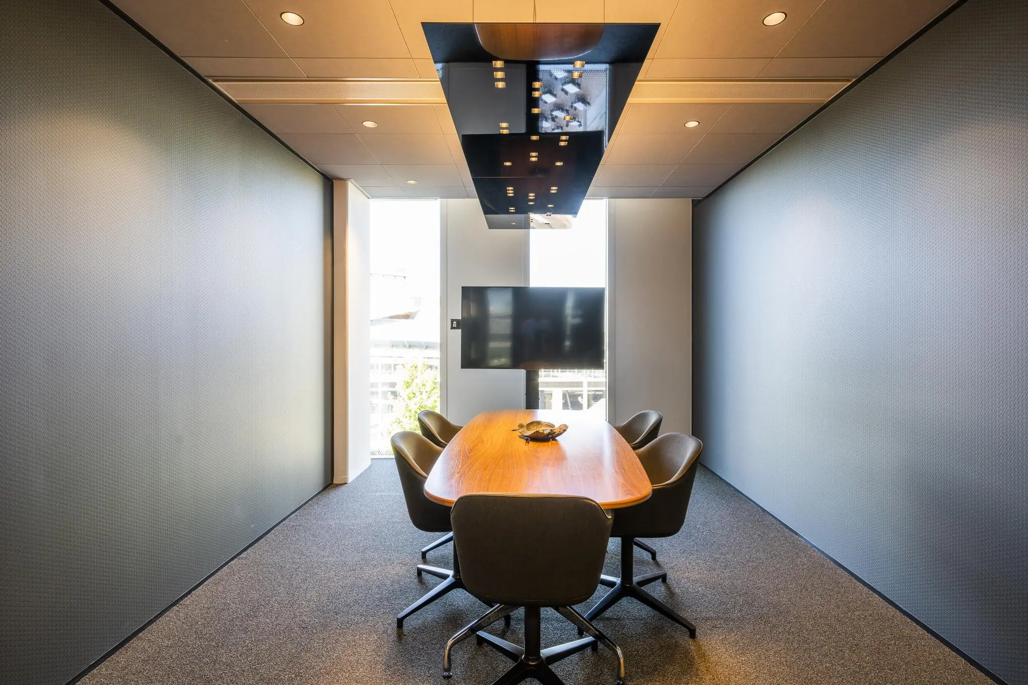 Moderne vergaderruimte in kantoorpand Hoekenrode met ovale houten tafel, vijf stoelen en een groot scherm aan de muur.