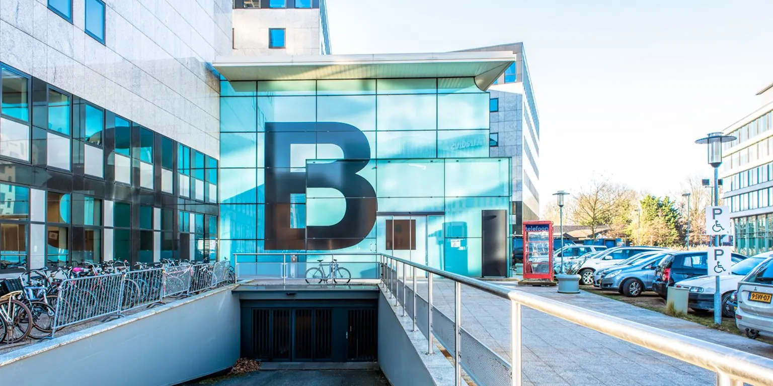 Glazen gevel van gebouw B aan het John M. Keynesplein met parkeerplaats en fietsenrek op de voorgrond.