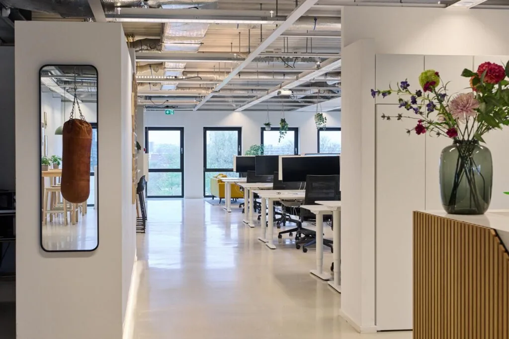 Modern kantoorinterieur aan het John M. Keynesplein met werkplekken, een boksbal en bloemen in een vaas.